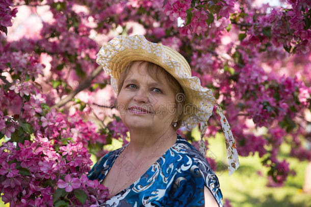 粉红花树下戴帽子的成年妇女