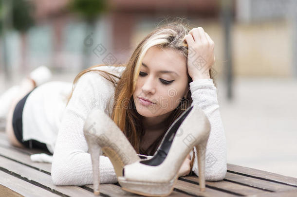 美丽优雅的年轻女人穿着高跟鞋躺在长凳上。