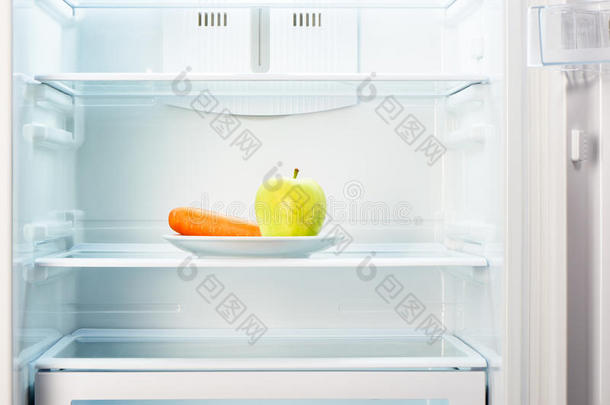 绿色苹果和橙色胡萝卜在白色盘子在开放的空冰箱