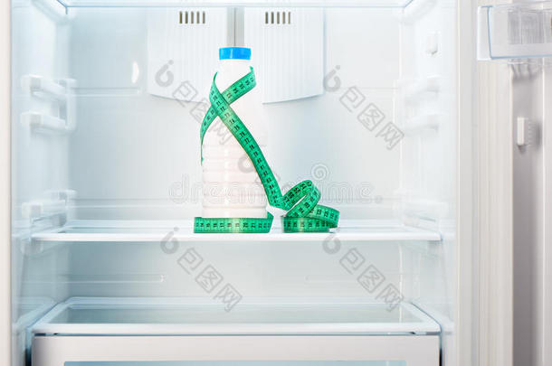 一瓶酸奶，在打开的空冰箱的架子上放着测量胶带