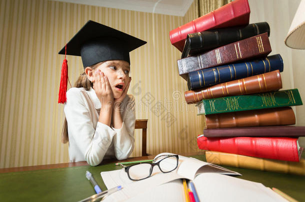 戴着毕业帽的女孩看着桌子上堆积如山的书