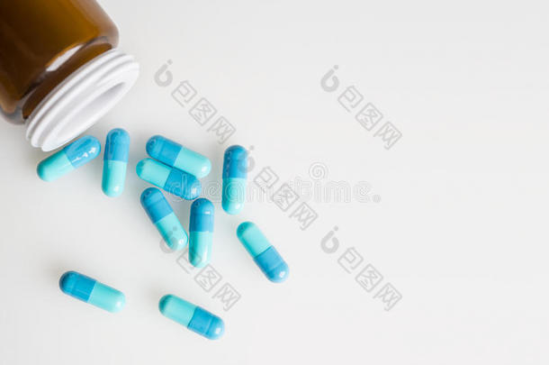 玻璃医疗瓶和蓝色药物胶囊，药丸洒在白色表面