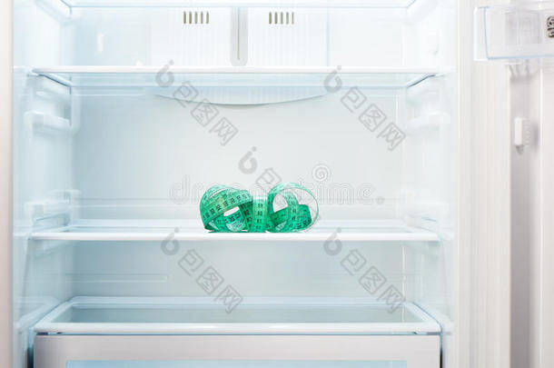 打开的空冰箱架子上的绿色测量胶带