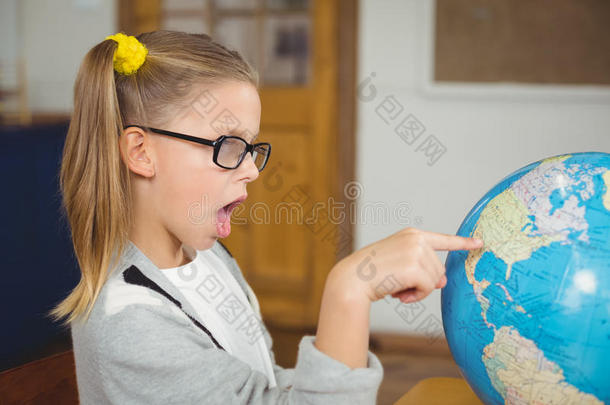 惊讶的小学生在教室里指着地球仪