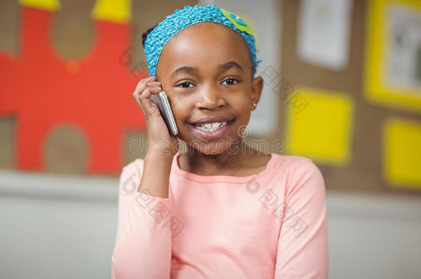 可爱的小学生在教室里用智能手机打电话