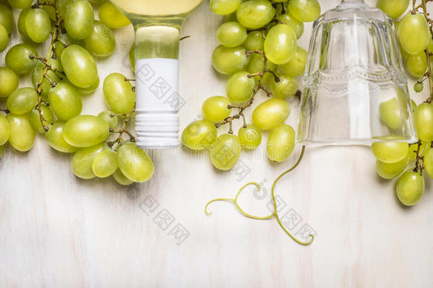 明亮的葡萄与一瓶白酒和玻璃在乡村白色的木制背景