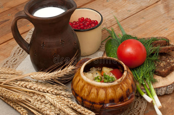 一种煮熟的蔬菜陶器，一罐牛奶，一块木板，木头表面有西红柿、黄瓜、面包和蔬菜