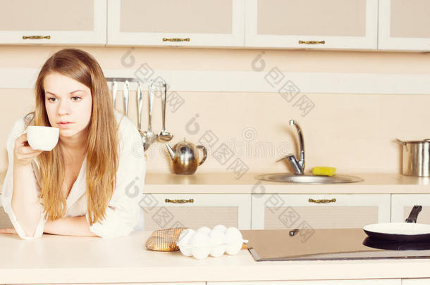 女孩白色男衬衫，长发飘逸，正在喝茶。 厨房。 早上好