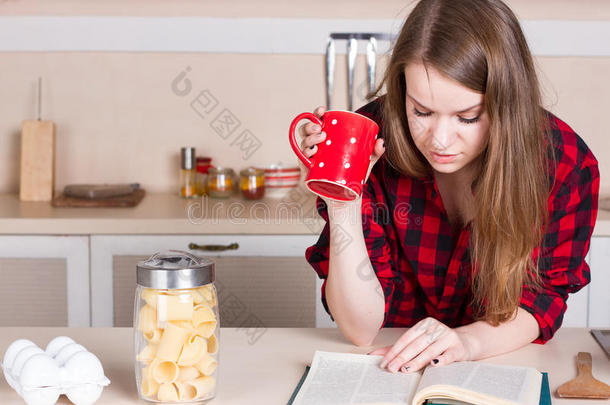 穿着红色衬衫的<strong>女孩喝茶</strong>读书。 厨房。 水平的