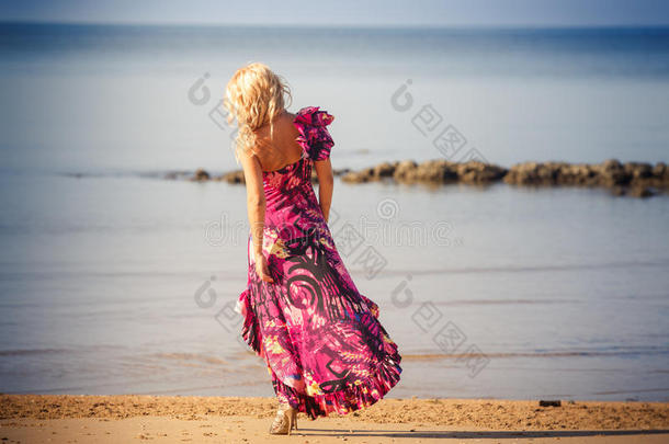 穿紫色连衣裙的金发女孩在海滩上散步
