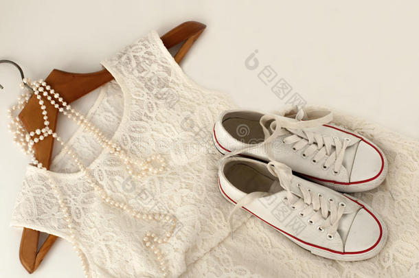 一件白色花边连衣裙，一双运动鞋在木制衣架上，一条珍珠项链在白色上