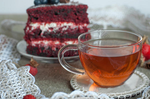 一杯茶和一个漂亮的自制蛋糕放在亚麻布表面，上面装饰着蓝莓、臀部、花边和肉桂枝