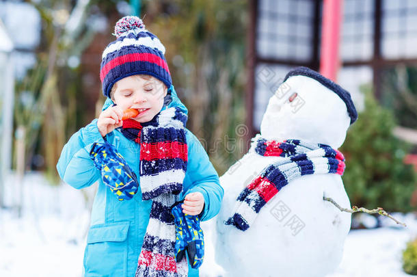 有趣的男孩穿着五颜六色的衣服在户外堆雪人