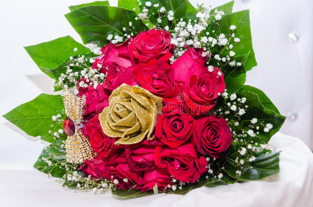 一束红色的新鲜玫瑰和金色的人造玫瑰，在白色的椅子上有丝带、珠子和绿叶