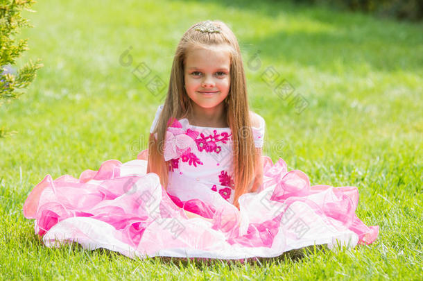 五岁的女孩穿着一件漂亮的衣服坐在绿色花园的草坪上