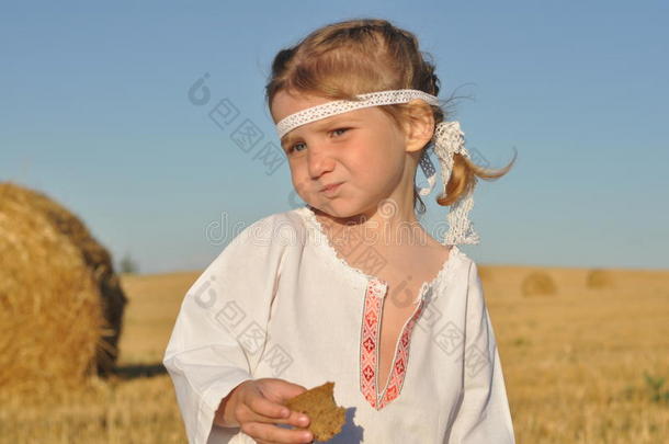 一个穿着斯拉夫传统服饰的小女孩在收获的<strong>田地</strong>里吃黑麦面包