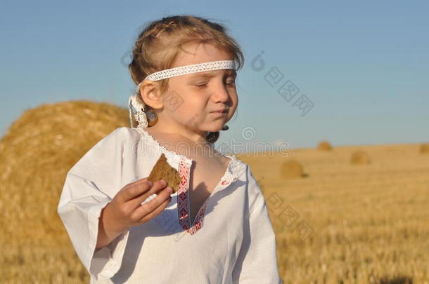 一个穿着斯拉夫传统服饰的小女孩在收获的田地里吃黑麦面包