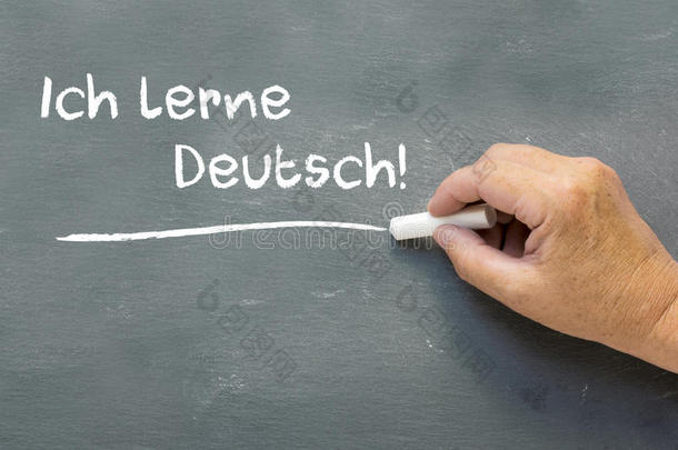 把手放在黑板上，上面写着德语单词ichLerneDeutsch(I