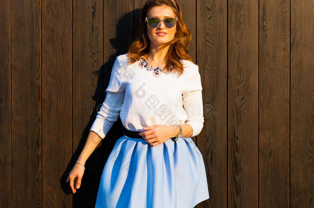 美丽时尚的女人戴着太阳镜，一条蓝色的短裙摆在温暖的<strong>夏天夜晚</strong>的木墙附近