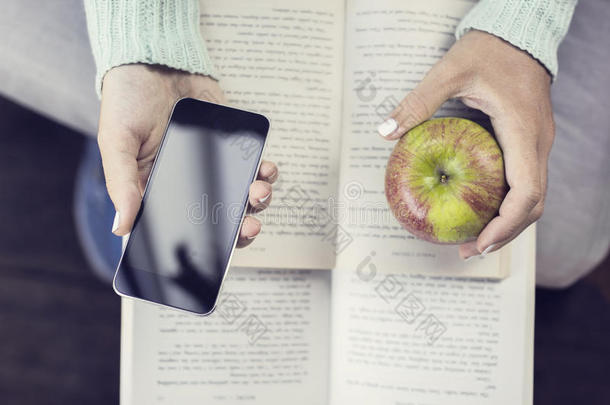 女孩的手保存智能手机，苹果和打开的书