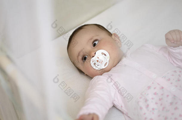 婴儿躺在婴儿床上，用白色奶嘴