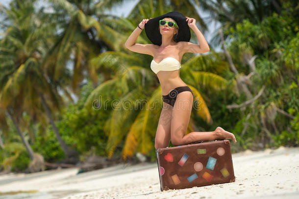 美丽的女孩在海滩上拿着一个老式的手提箱