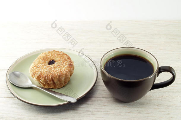 黑咖啡在深棕色陶瓷杯和棕色杯蛋糕与银金属茶匙在陶碟在木制桌面