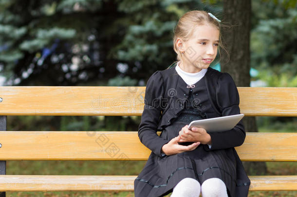 可爱的年轻学生女孩坐在公园里的平板电脑