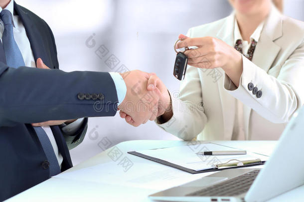 汽车推销员把一辆<strong>新</strong>车的钥匙交给一位年轻的商人。 两个商人之间的握手