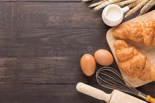 木制背景上新鲜烘焙的牛角面包、牛奶和鸡蛋