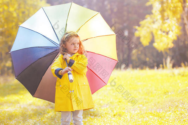 可爱的小女孩穿着黄色夹克，带着五颜六色的雨伞