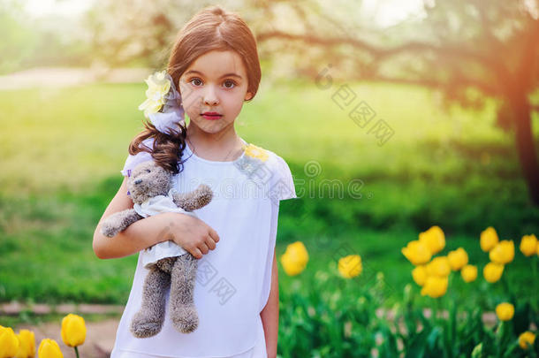 可爱惊讶的女孩抱着泰迪熊在春天散步，背景是黄色郁金香
