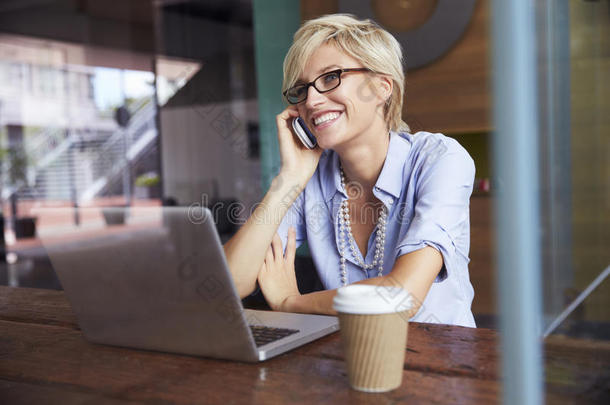 女商人在<strong>咖啡店</strong>用手机在笔记本电脑上工作