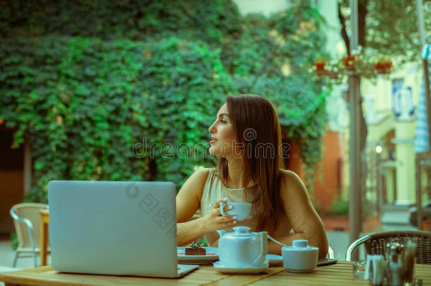 迷人的年轻女孩带着笔记本电脑和一杯茶<strong>看</strong>着<strong>远方</strong>