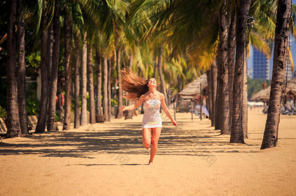 穿着<strong>蕾丝花边</strong>的金发女孩赤脚在海滩上的手掌之间奔跑