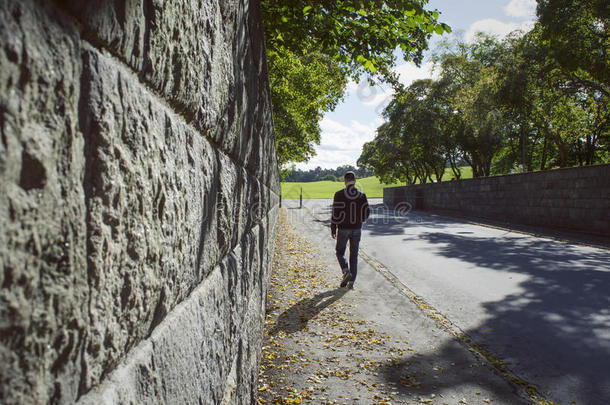 沿着石墙和一个在秋天的街道上行走的人的深邃视角。