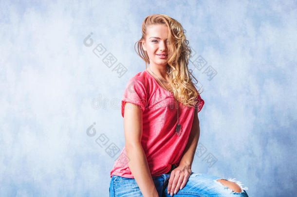 金发女孩微笑着坐着，穿着<strong>粗犷</strong>的牛仔裤和凌乱的头发