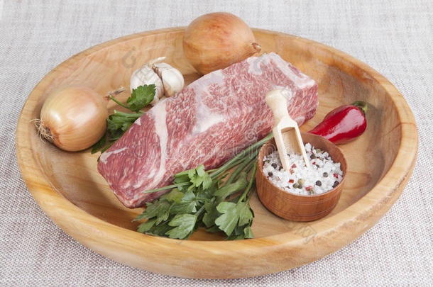 一块新鲜的大理石牛肉，辣椒，欧芹，洋葱，大蒜，肋骨躺在木托盘上