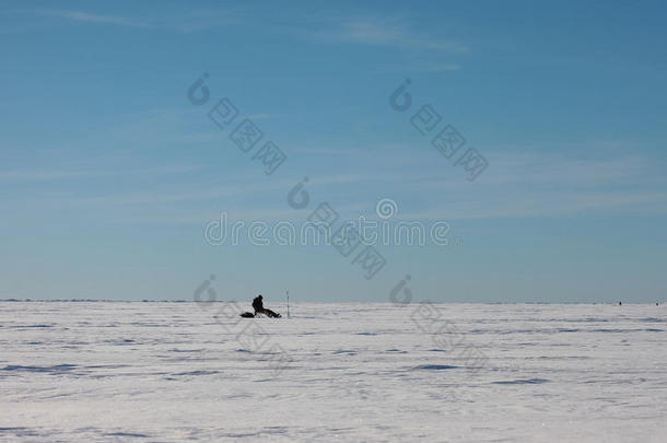 雪原上孤独的渔夫。冬季海面上的蓝天