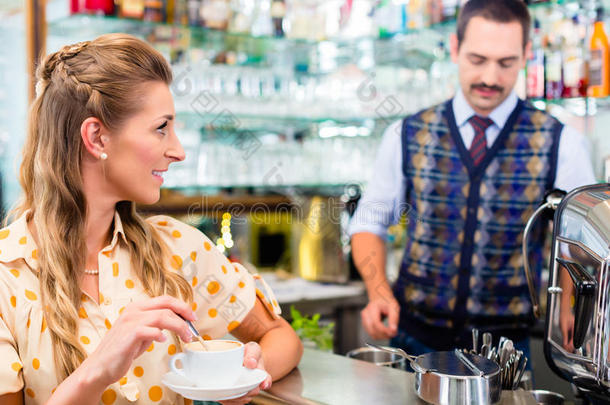 女孩在咖啡馆或酒吧搅拌咖啡杯，咖啡师在后面