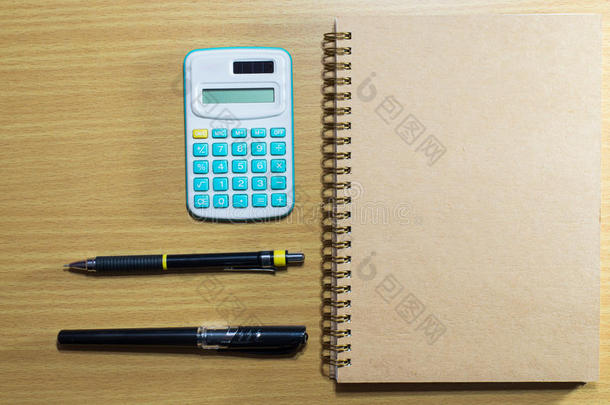 木制桌子上的计算器、钢笔、铅笔和笔记本。 上面的风景