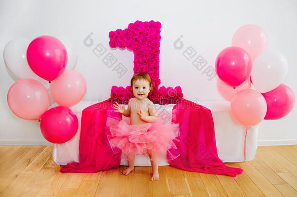 一岁生日。婴儿穿着蓬松的粉红色裙子，带着气球和一双