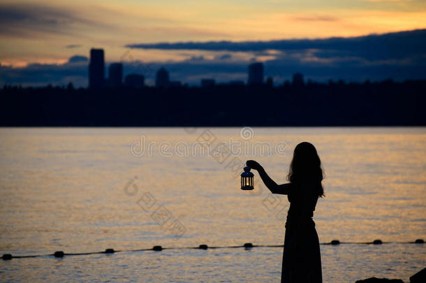 美丽的年轻女人，拿着灯笼，在小树枝上等待着湖面