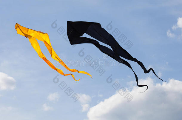 黑色和黄色的风筝在多云的天空中飞翔。 夏天的概念
