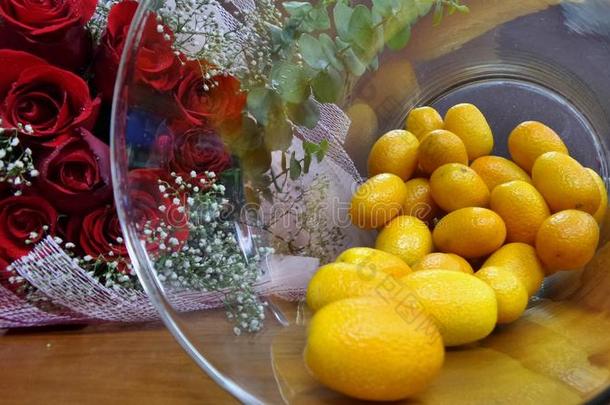 新鲜的<strong>金橘</strong>橙在玻璃瓶和红玫瑰花束在木地板上