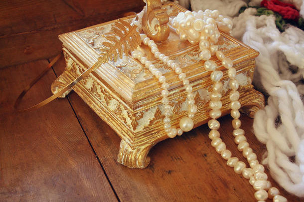 一个美丽的古董<strong>黄金珠宝</strong>盒，木制桌子上有天然的白色珍珠。 复古过滤图像