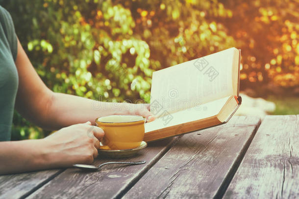 一个女人在户外看书的特写镜头，在下午的木桌和咖啡杯旁。过滤后的图像。过滤后的图像