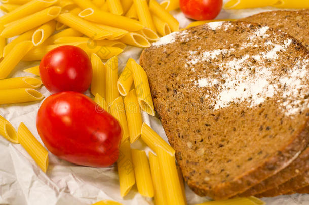 近景的面包片洒上面粉，意大利面食和西红柿在白纸上