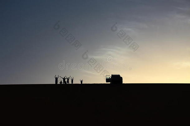 一群<strong>冒险者</strong>在埃及达赫拉绿洲享受美丽的夏季日落时，从一个大沙丘的顶部敬礼