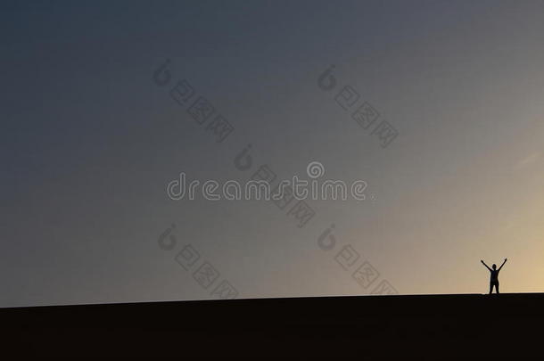 一位孤独的冒险家在埃及达赫拉绿洲享受美丽的夏季日落时，从一处宏伟的沙丘顶部向人们致敬